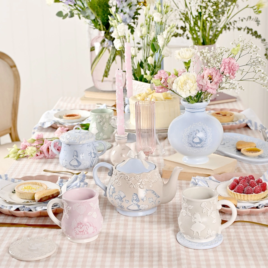 Gedekte tafel met de Alice in Wonderland-theepot, mokken en een vaas in pastelblauw en roze